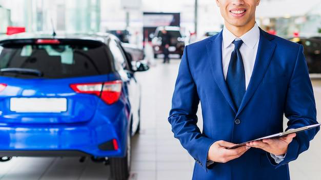 A person wearing a suit and holding a clipboard with a car in the background