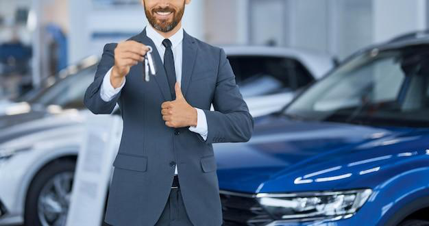 A car dealership representative holding car keys and a thumbs up